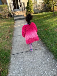 a little girl walking down a sidewalk in a pink fur coat