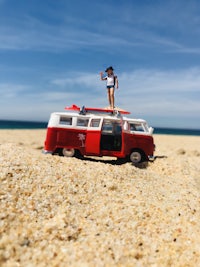 a girl is standing on top of a red van on the beach