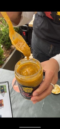 a person dipping a spoon into a jar of mustard