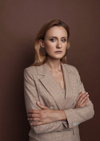 a woman in a brown suit posing with her arms crossed