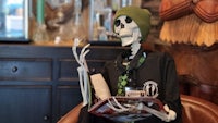 a skeleton sitting in a chair holding a cigarette