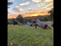 a group of people doing push ups in the grass at sunset