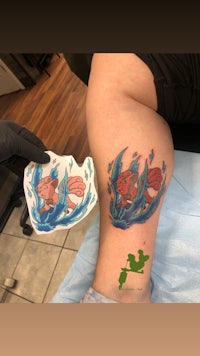 a woman is getting a tattoo of a fish on her leg
