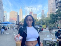 a woman in a crop top and jeans holding a drink in front of a city