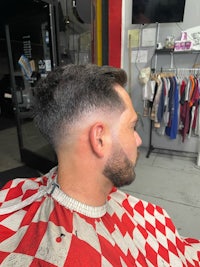 a man sitting in a barber shop with a red and white checkered shirt