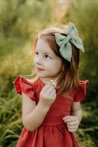 a little girl in a red dress holding a flower