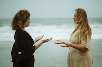 two women standing on the beach talking to each other