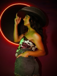 a woman in a cowboy hat standing in front of a neon wall