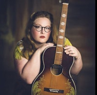 a woman with glasses holding an acoustic guitar