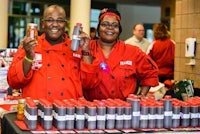 two people in red jackets standing next to a table full of cans