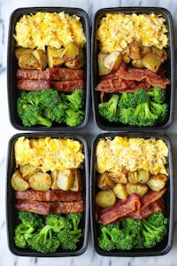 four black plastic containers with bacon, eggs, broccoli and potatoes