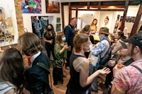 a group of people standing in a room with paintings on the wall