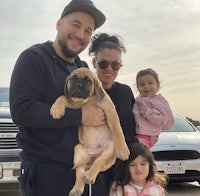 a man and woman pose with a dog in a parking lot