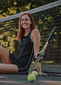 a young woman sitting on a tennis court with a tennis racket