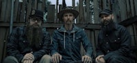 three men with beards and hats sitting in front of a fence