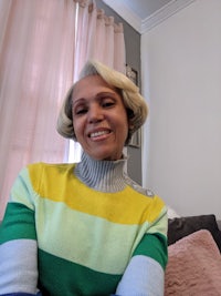 a woman sitting on a couch wearing a multicolored turtleneck sweater