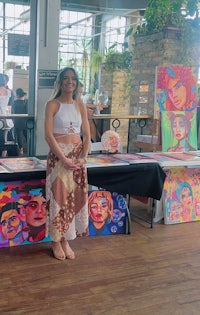 a woman standing in front of a table full of paintings