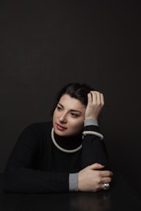 a woman in a black sweater leaning against a black background
