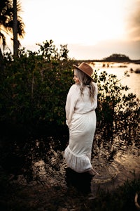 a woman in a white dress standing in the water at sunset