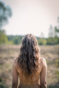 a woman with long curly hair standing in a field