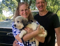 a man and woman holding a white puppy in front of a truck