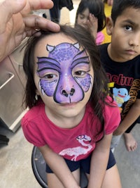 a little girl with a purple face painted on her face