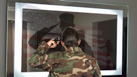 a man in camouflage holding a gun in front of a mirror
