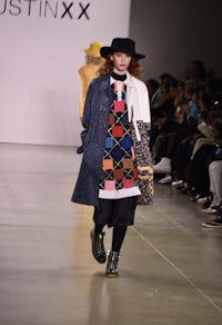 a woman walks down the runway wearing a hat and coat