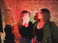 two women covering their faces in front of a brick wall