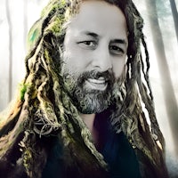 a man with dreadlocks smiling in the woods