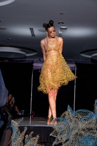 a woman in a gold dress on a runway