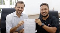 two men are smiling while holding up a piece of paper