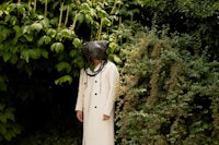 a person in a white coat standing next to bushes