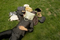 a man laying on the grass with a lot of purses