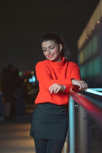 a woman in a red sweater leaning on a railing at night