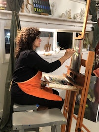 a woman in an orange apron is painting on an easel