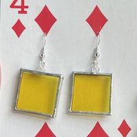 a pair of yellow square earrings on a playing card