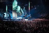 a large crowd at a concert with a large screen in the background