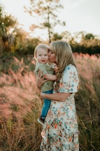a woman kisses her son in a field at sunset
