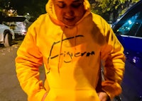 a man in a yellow hoodie standing next to a car