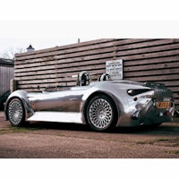 a silver sports car parked in front of a wooden fence