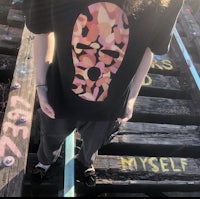 a man wearing a camouflage t - shirt standing on a bridge