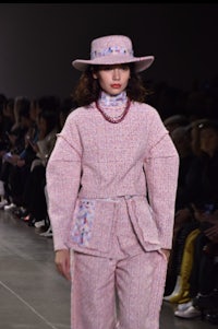 a model walks down the runway in a pink suit and hat