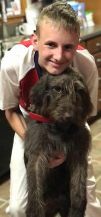 a young boy holding a dog in a kitchen
