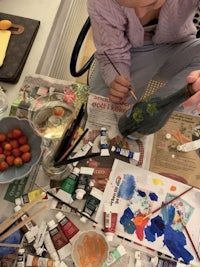 a woman is painting on a table with paints and brushes