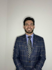 a man in a suit and tie smiles in front of a white wall