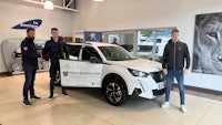 three men standing next to a white suv in a showroom