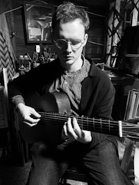 a man in glasses playing an acoustic guitar