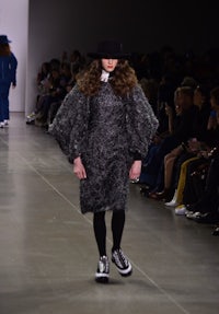 a model walks down the runway wearing a black coat and hat