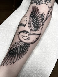 a black and white tattoo of a bird on the forearm